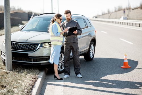 Woman with road assistance worker signing some documents standing near the car in road accident on the highway