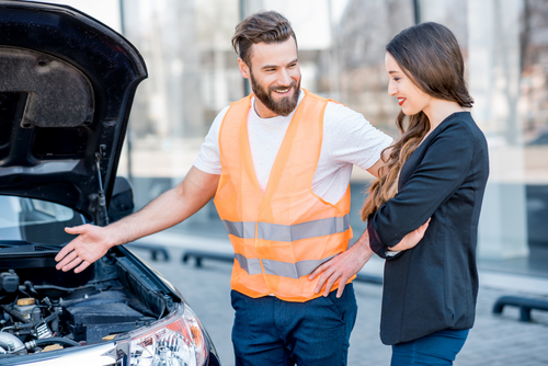 Handsome service worker consulting or providing technical assistance of the broken car to the businesswoman standing near the service center building